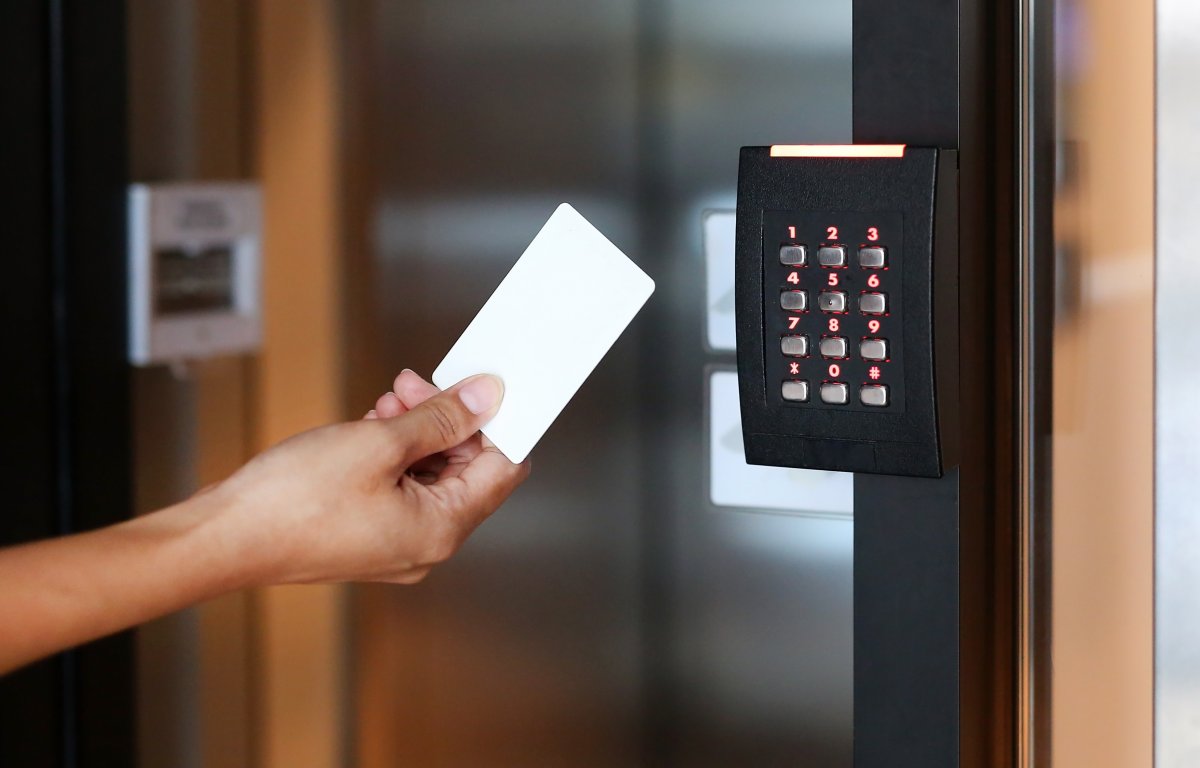 A person holding a white key card near an electronic keypad access control system to unlock a secure door.